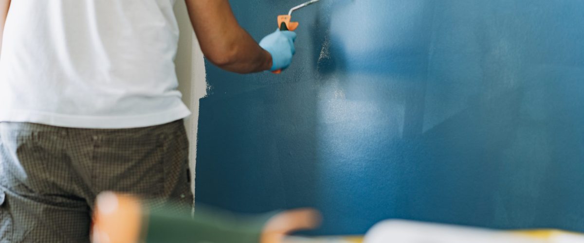 caucasian bearded man painting wall with paint roller. Painting apartment, renovating home with blue color paint. Image with selective focus