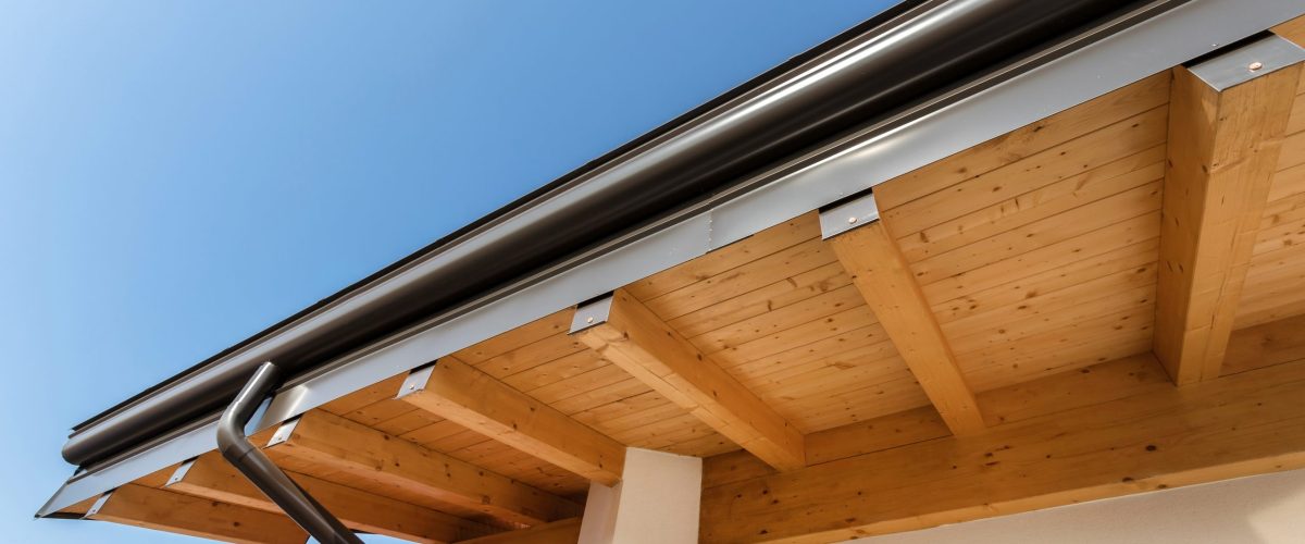 New wooden warm ecological house roof with steel gutter rain system. Professional construction and drainage pipes installation. Eco materials.